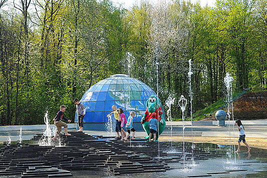 Kinder spielen und planschen zwischen Wasserfontänen des Galaktischen Nebels im Saurierpark